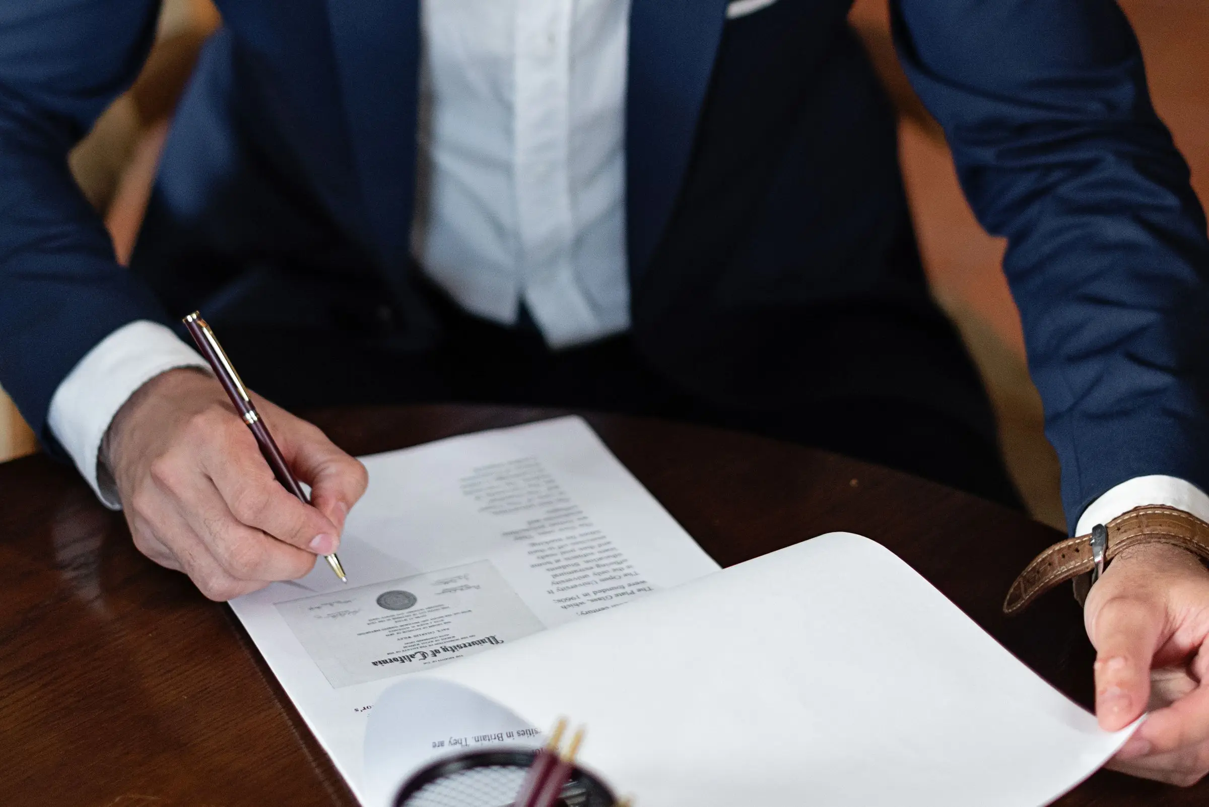 Person in a suit signing legal papers at a desk